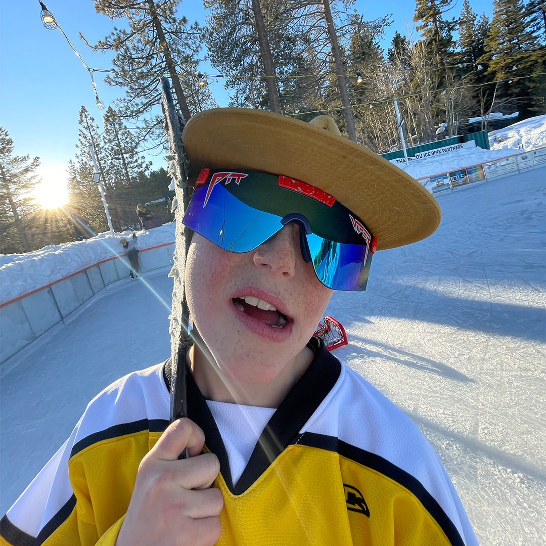 Kid holding a hockey stick wearing blue sunglasses with a red frame - lifestyle